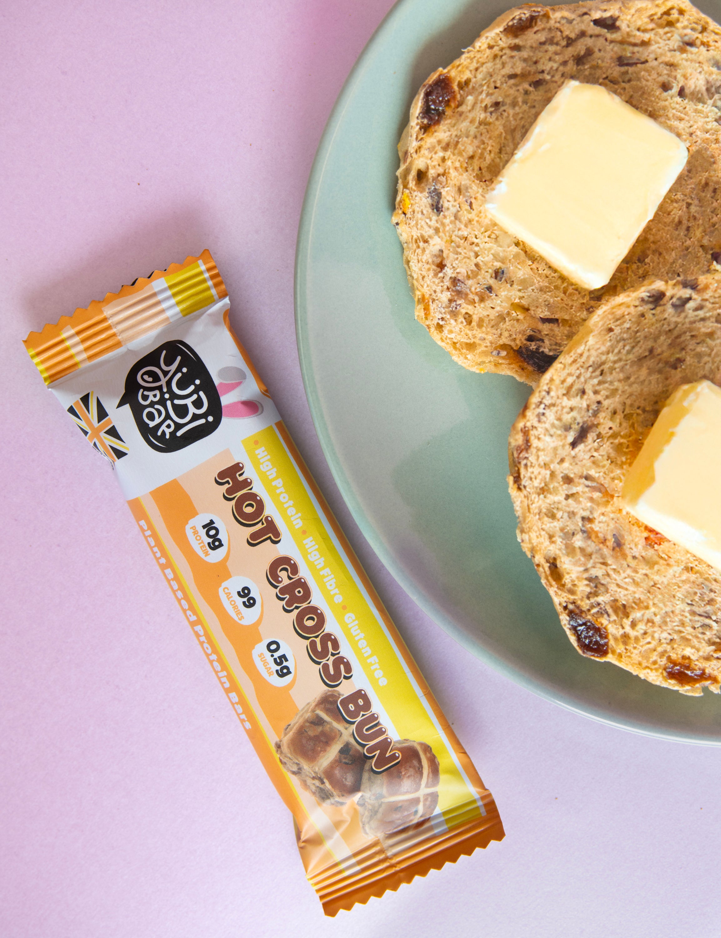 Hot Cross Bun protein bar with easter bunny ears next to a plate of hot cross buns