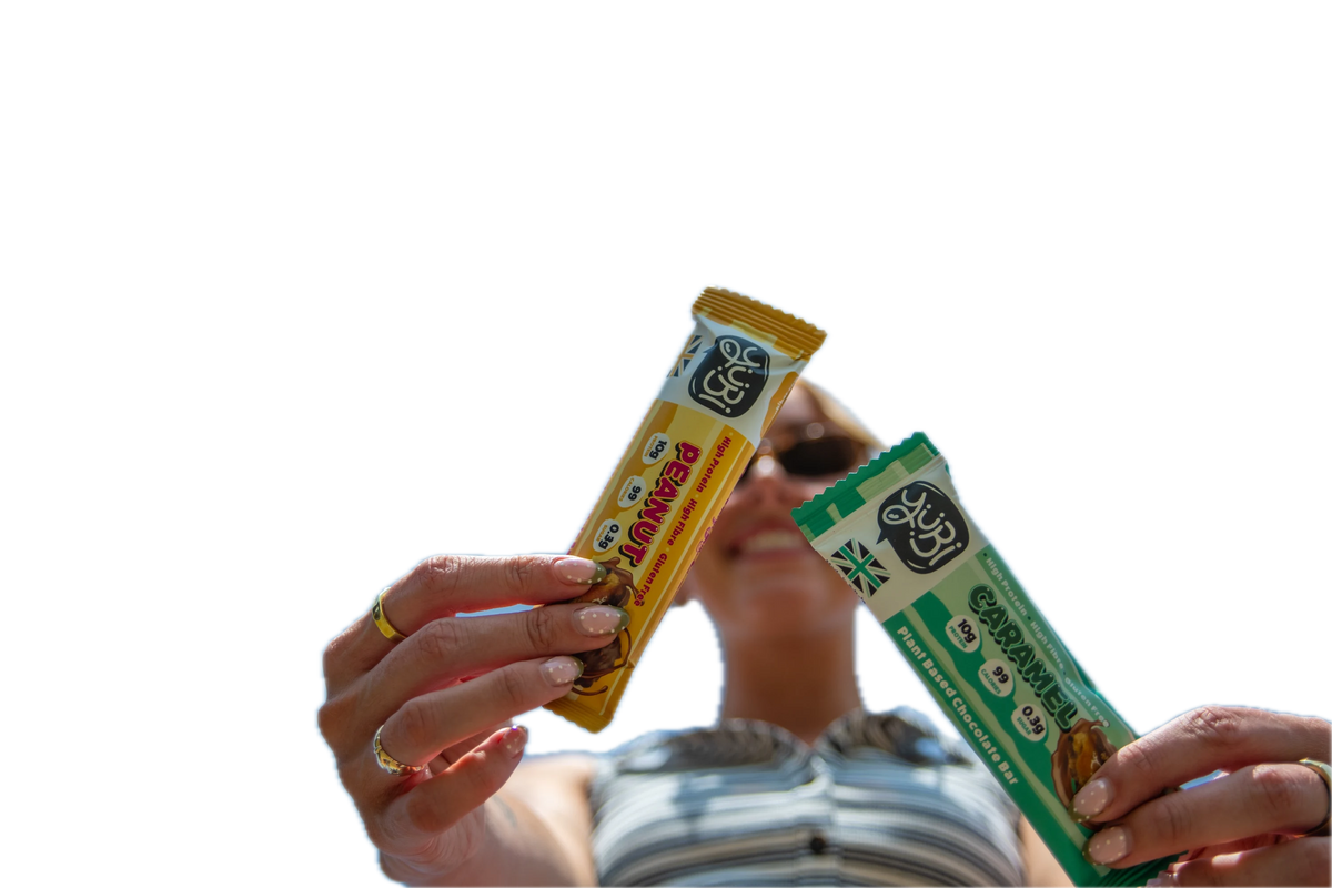 Holding up YuBi Peanut and Caramel protein bars against a bright blue sky